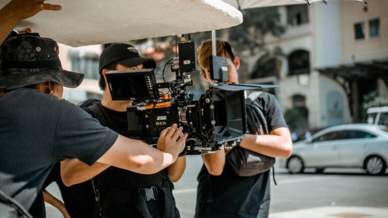 Three students looking through a film camera on the street.