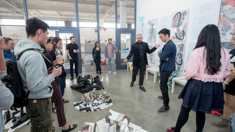 A USC School of Architecture is standing and speaking to students about models on the floor, while students stand around and listen.