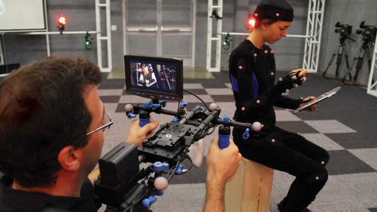A man filming an actress that is wearing a body suit with motion sensors attached to it.