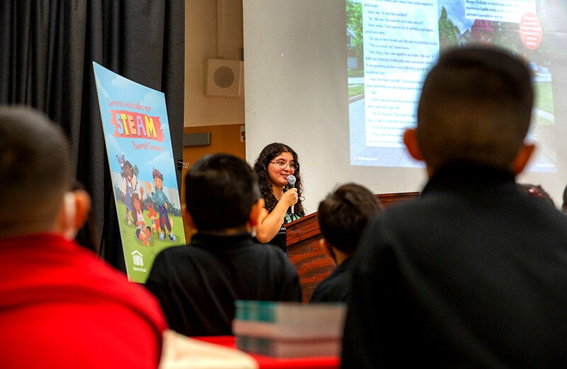 A young woman speaking in front of a podium to young students.