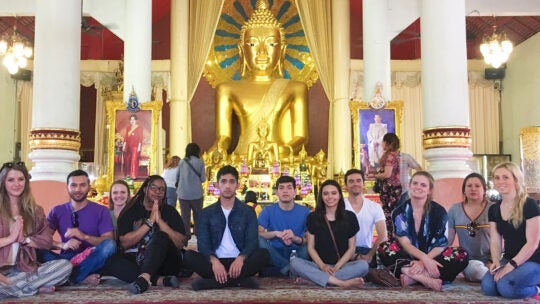 USC students sit on the floor in front of a statue of the Buddha in Thailand.