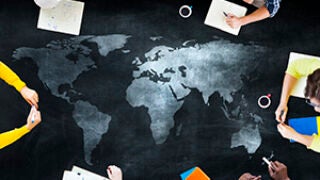 Students writing notes over a large map of the world on the ground