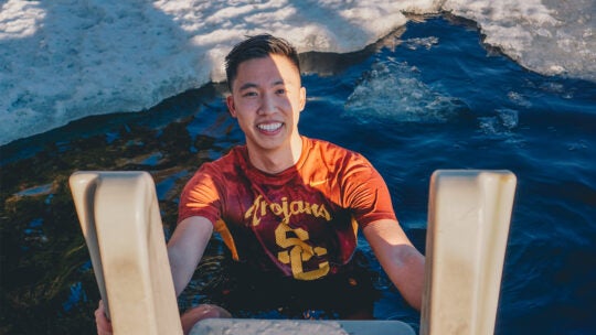 A USC student wearing a Trojans SC t-shirt prepares to descend from a boat into the water.