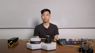 USC Annenberg doctoral student sits in front of a desk with his invention that bridges the electronic and classical music worlds