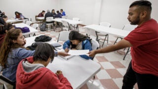 Teacher working with students in a classroom with tables and chairs