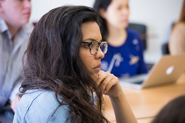 A student with long hair and glasses listens attentively in a classroom at the USC Annenberg School for Communication and Journalism.