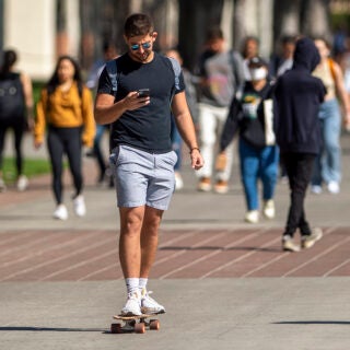 Male student on skateboard looking at his phone