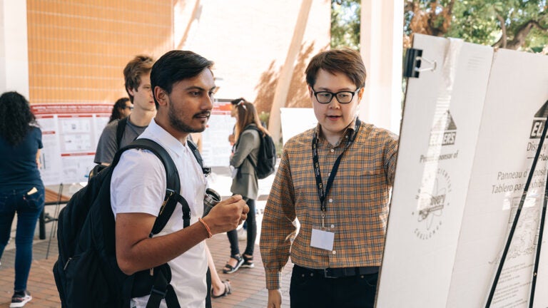 Students and faculty read a posterboard at the 2022 Inaugural Astani Research symposium.