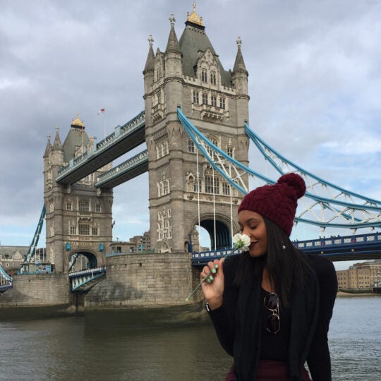 A USC student smells a white flower in front of London Bridge.