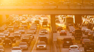 Cars in traffic on a highway with the sun setting.