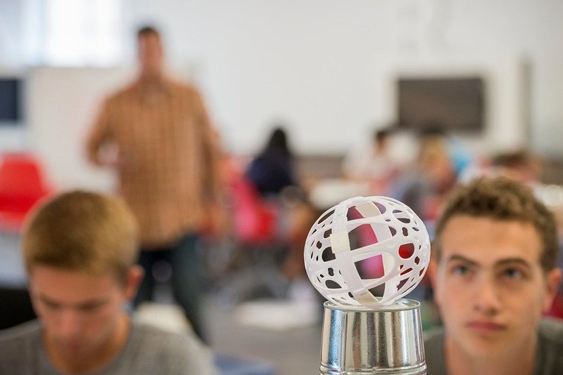 Students stare at white plastic globe on top of a cylinder silver container