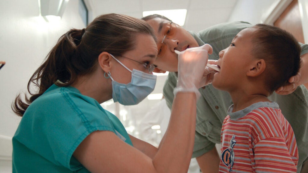 Doctor inserting popsicle stick in child's mouth to examine him