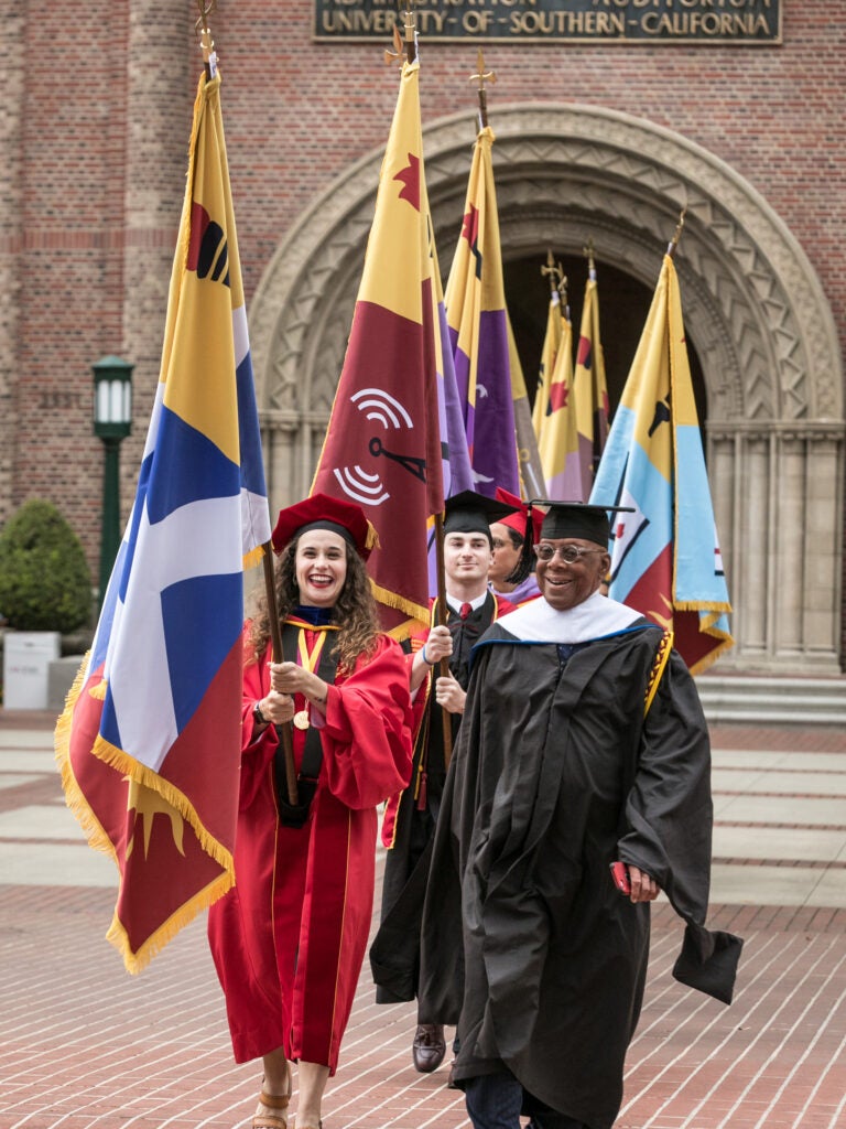 Flag bearers wearing graduation regalia process at a USC commencement ceremony.