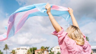 A person with blonde hair raises up a blue and pink fabric in the wind.