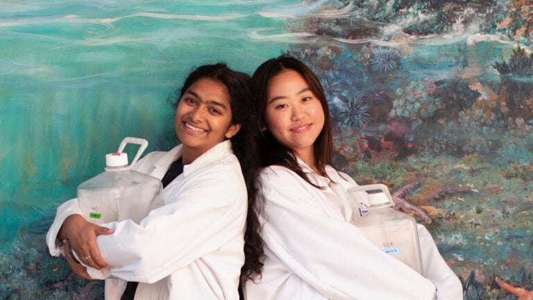 two students in lab coats holding research gear