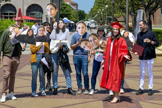 USC PhD graduating student with family holding up photos of her face