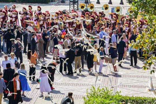Doves fly over USC's campus with a crown and Trojan Marching Band behind