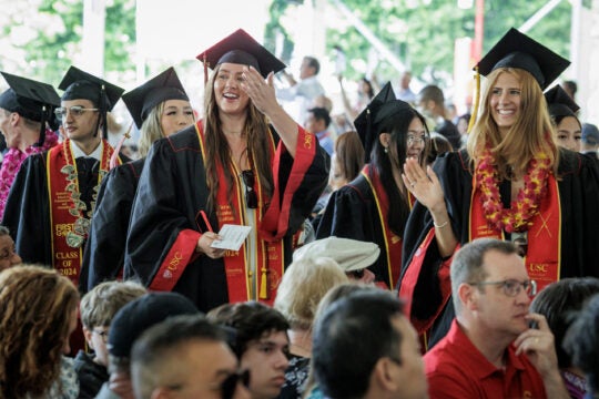 Students waving to their families as they walk to their seats for their grad ceremony