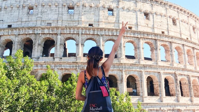 Shot from behind of a student holding up the Trojan fight on sign in front of the Coliseum in Rome