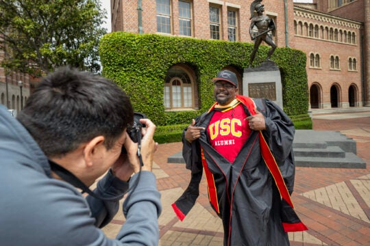 Rick Jones poses for a photograph with his USC alumni shirt under robes