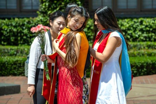 A fellow graduating student assist another with her sash