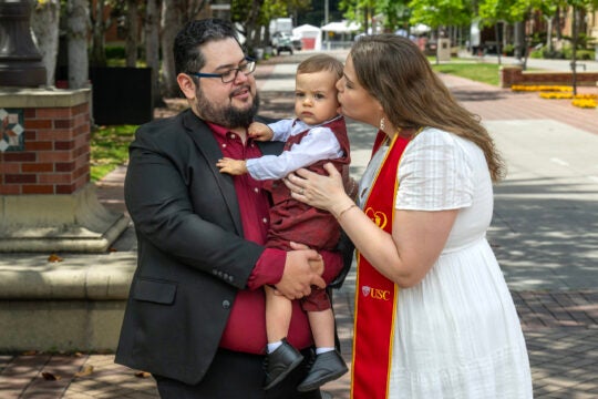 a graduate and her partner kissing their child