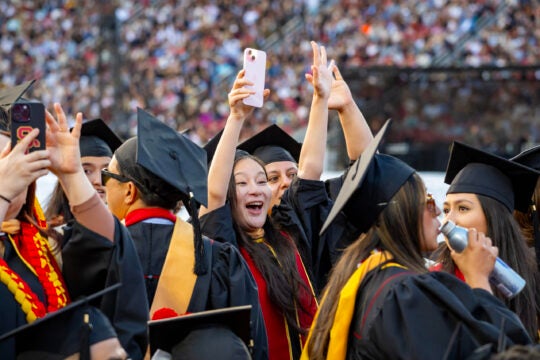 USC graduates smile with hands in the air