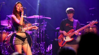 A female student sings on stage while a male student plays guitar in the background
