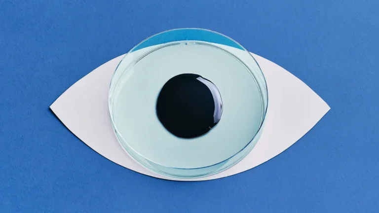 Petri dish filled with pale blue liquid and a dark circular sample, arranged to resemble an eye on a blue background.